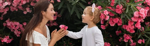 Вид сбоку жизнерадостной девочки, дающей цветы матери рядом с растением в Валенсии, баннер — стоковое фото