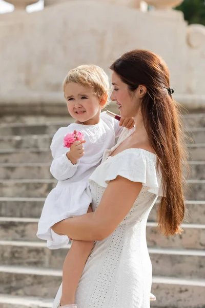 Mother looking at baby daughter holding flowers and lip gloss in Valencia — Stock Photo