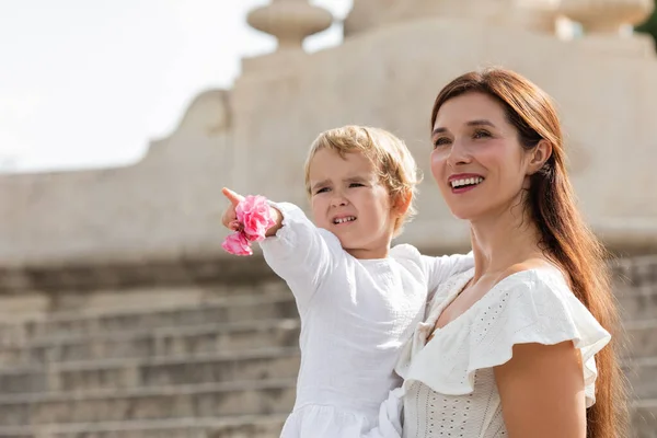 Baby girl holding flowers and pointing with finger near mom in Valencia — Photo de stock