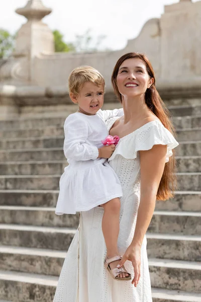 Lächelnde Frau hält Baby-Mädchen mit rosa Blumen in Valencia — Stockfoto