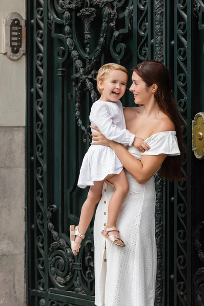 Donna sorridente che tiene in braccio la figlia neonata vicino al palazzo in strada a Valencia — Foto stock