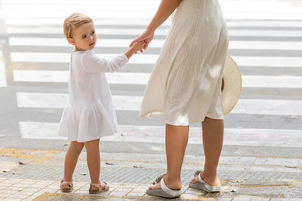 Toddler girl holding hand of mom with straw hat near crosswalk in Valencia — Stock Photo
