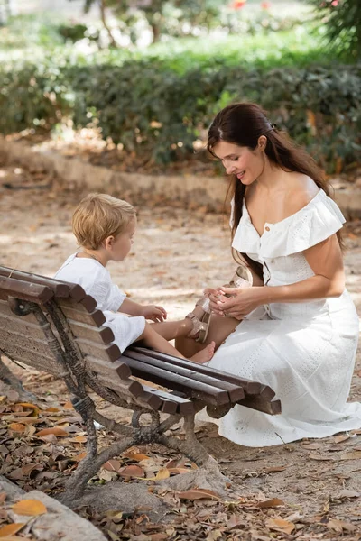 Smiling woman taking off sandal from toddler daughter on bench in park in Valencia — Stock Photo