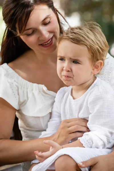 Smiling mother looking at sad baby daughter in park — Stock Photo