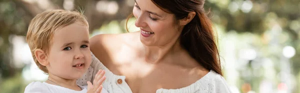 Мать смотрит на улыбающегося ребенка в летнем парке, баннер — стоковое фото