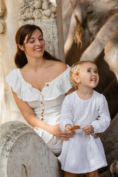 Fröhliche Frau hält Kleinkind-Tochter mit Blatt in Park in Spanien — Stockfoto