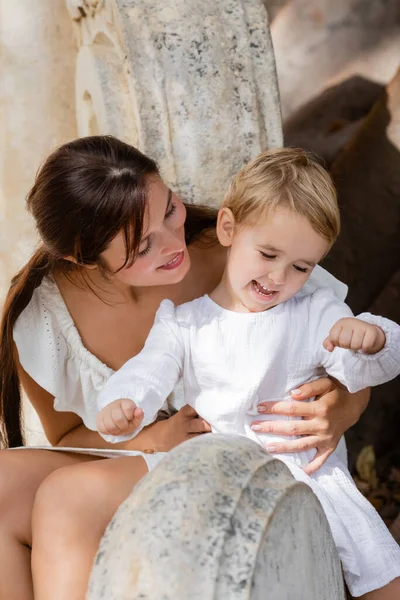 Fröhliche Mutter im Kleid umarmt Tochter auf Steinbank in Valencia — Stockfoto