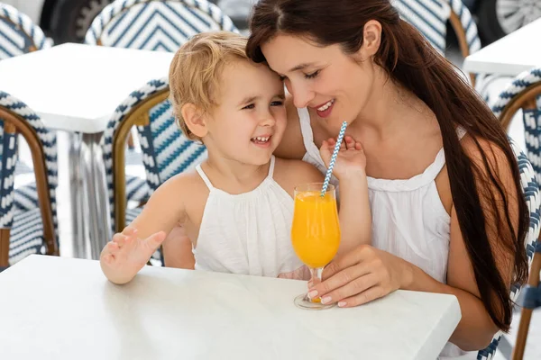 Woman hugging baby daughter near orange juice on table in outdoor cafe in Valencia — Stockfoto