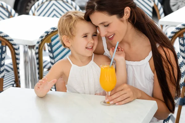 Woman hugging baby daughter near orange juice on table in outdoor cafe in Valencia — Stock Photo