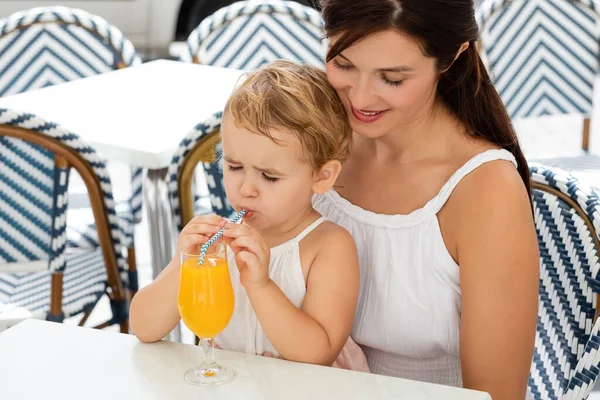 Parent looking at baby daughter drinking orange juice in outdoor cafe in Spain — Stock Photo