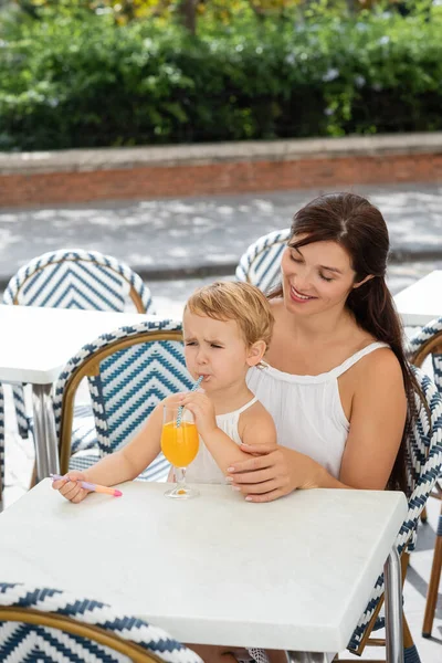 Cheerful mom looking at toddler girl drinking orange juice in outdoor cafe in Valencia — Stock Photo