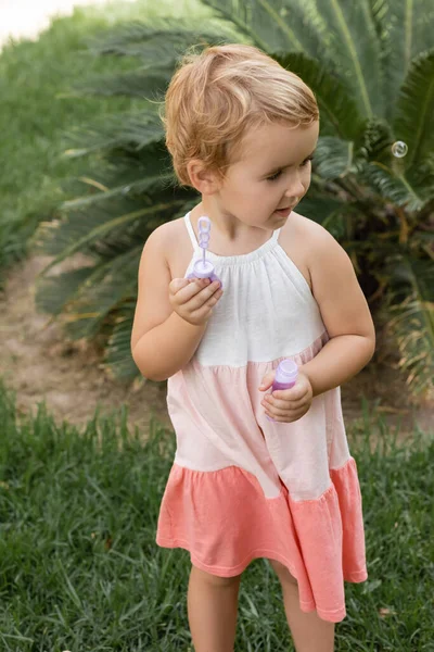 Toddler child in summer dress holding soap bubbles on lawn — Stock Photo
