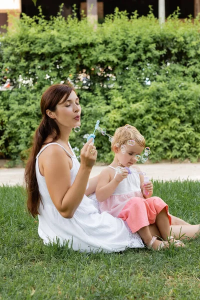 Mother and child blowing soap bubbles on meadow in park — Stock Photo