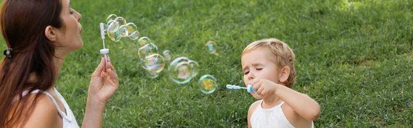 Mother and baby girl blowing soap bubbles in summer park, banner — Stock Photo