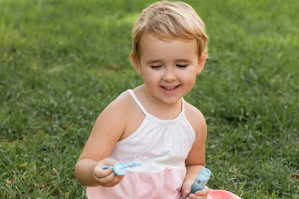 Positive toddler kid playing with soap bubbles on grass in park — Stock Photo