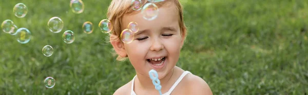 Веселая девочка держит палочку возле мыльных пузырей в парке, баннер — стоковое фото