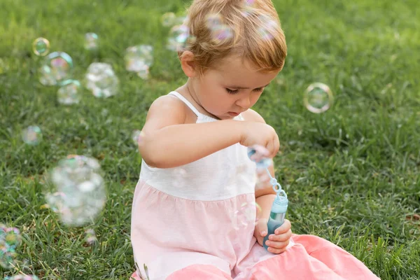 Focused baby girl holding soap bubbles on grass in park — Stock Photo