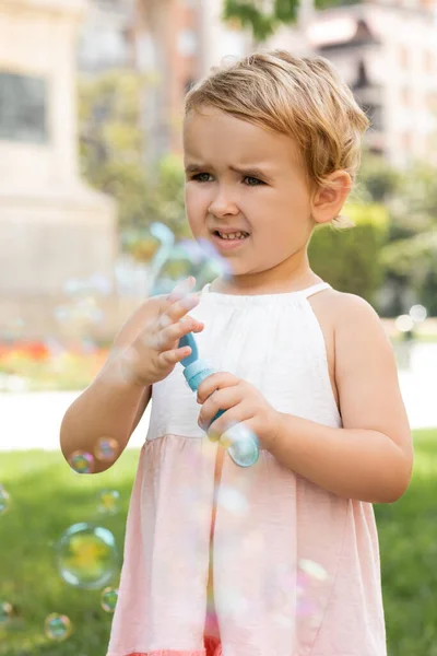 Портрет сфокусированной девочки в платье с мыльными пузырями в парке — стоковое фото