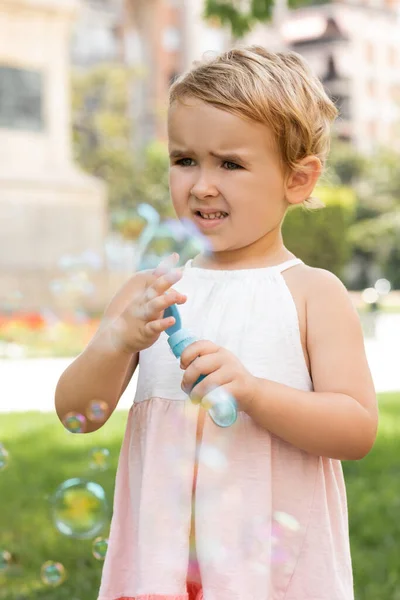Portrait of focused baby girl in dress holding soap bubbles in park — Stock Photo