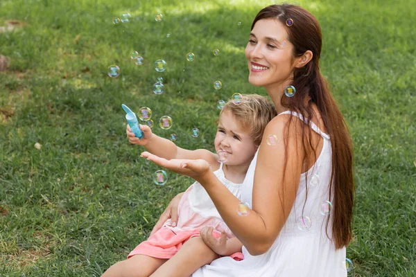 Positive mother and toddler child playing with soap bubbles in summer park — Stock Photo