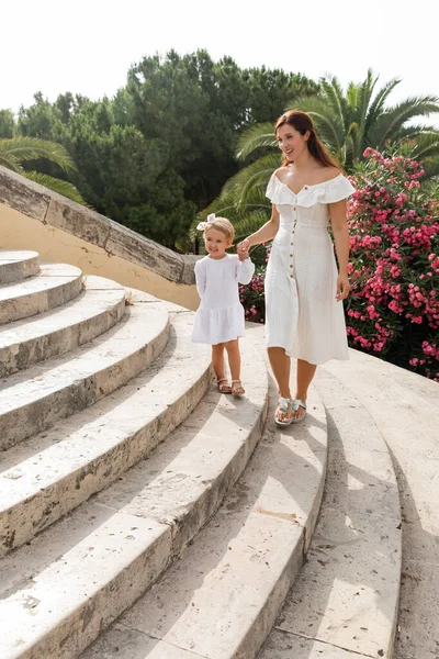Woman and daughter in white summer dresses walking on stairs of Puente Del Mar bridge in Spain - foto de stock