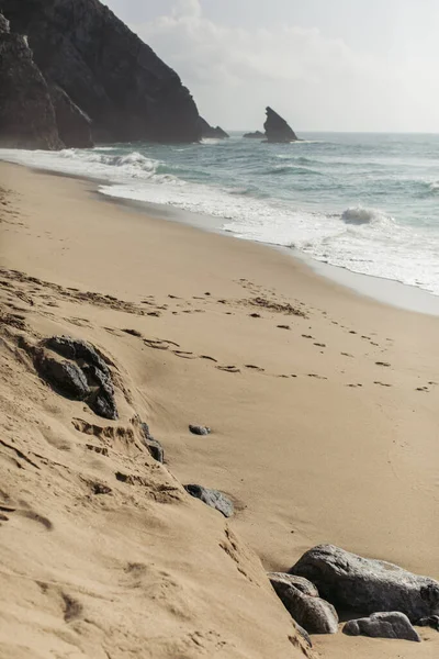 Камни на мокром песчаном европейском пляже возле океана в Португалии — стоковое фото