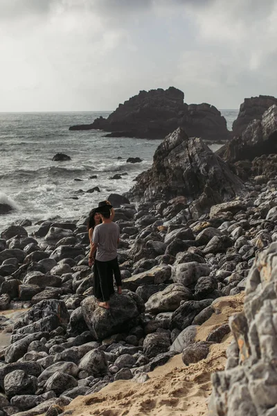 Frau trägt Hut auf Freund, während sie auf Felsen in Meeresnähe steht — Stockfoto