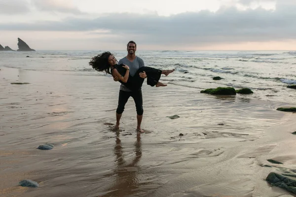 Homme heureux soulevant petite amie joyeuse sur la robe tout en se tenant sur l'eau de l'océan — Photo de stock