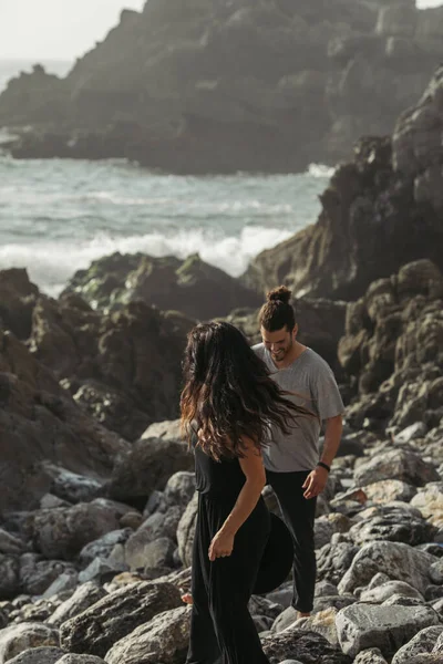 Happy man smiling while walking on rocks near tattooed girlfriend in dress — Stock Photo