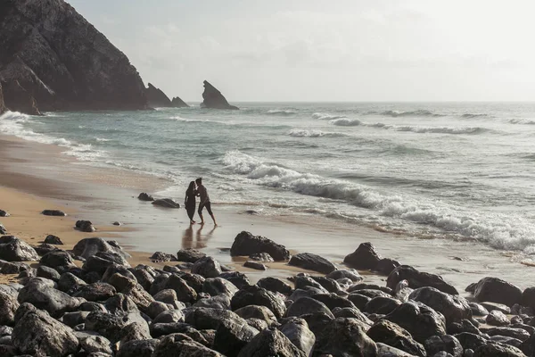 Bearded man hugging girlfriend in dress while walking in ocean water — Stock Photo