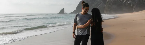 Happy man dancing with girlfriend in dress on wet sand near ocean, banner — Stock Photo