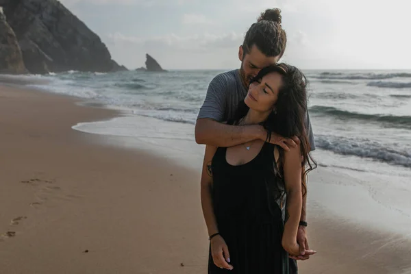 Happy man hugging tattooed girlfriend in dress near ocean in portugal — Stock Photo