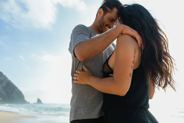 Feliz barbudo hombre abrazando morena novia cerca del océano durante las vacaciones - foto de stock