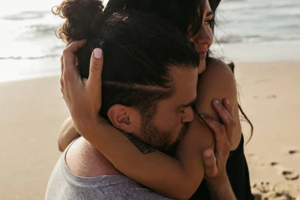 Bearded man kissing hand on happy woman with tattoo on beach — Stock Photo