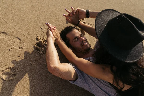 Draufsicht eines bärtigen Mannes, der Hände mit Frau im Hut hält und auf Sand liegt — Stockfoto