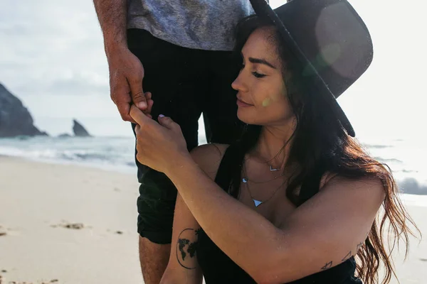 Man standing behind tattooed girlfriend in hat and holding her finger near ocean — Stock Photo