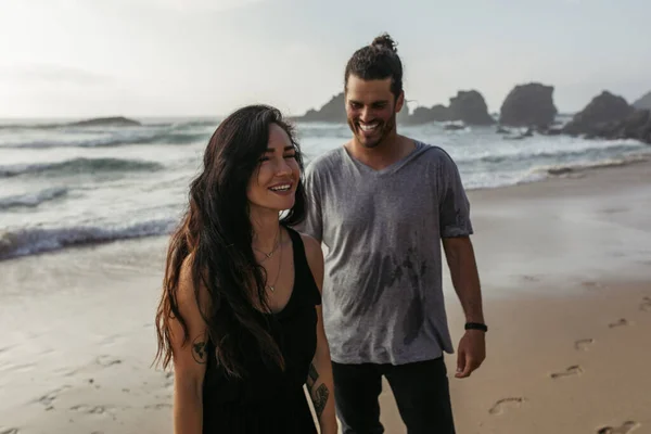 Happy and tattooed woman smiling near cheerful boyfriend on beach — Stock Photo