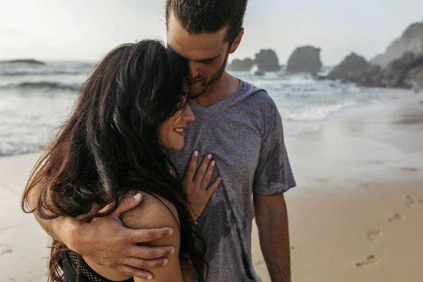 Бородатый мужчина в серой футболке обнимает счастливую подружку возле океана в Португалии — стоковое фото