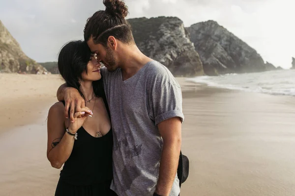 Joyful bearded man and tattooed woman in dress holding hands near ocean — Stock Photo