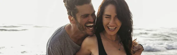 Cheerful man laughing near joyful girlfriend with closed eyes near ocean, banner — Stock Photo