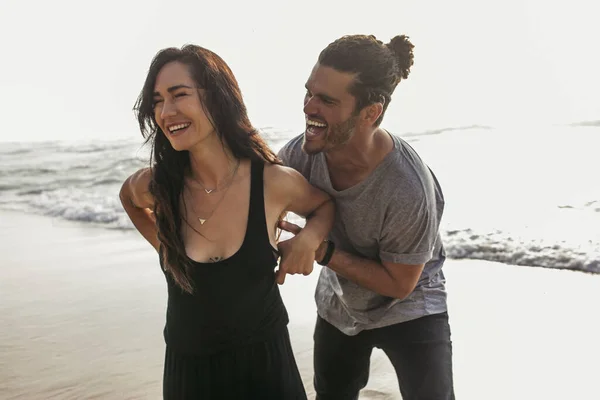 Весёлый мужчина щекочет улыбающуюся девушку в платье возле океана в Португалии — стоковое фото