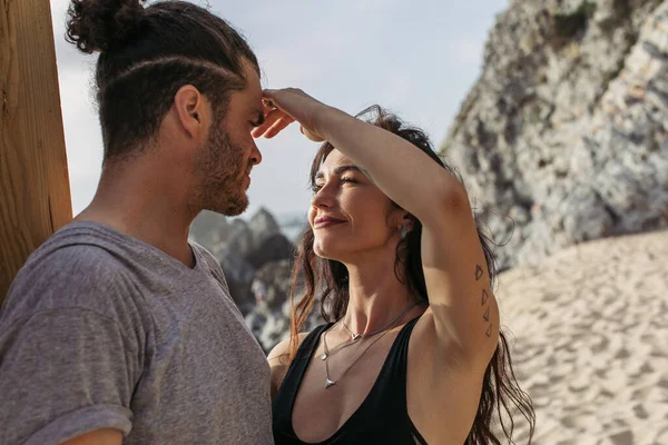 Tattooed woman touching face of bearded boyfriend on beach in portugal — Stock Photo