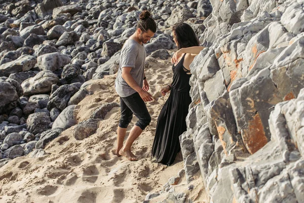 В полный рост мужчина и женщина в платье стоят вместе на скальном пляже — стоковое фото