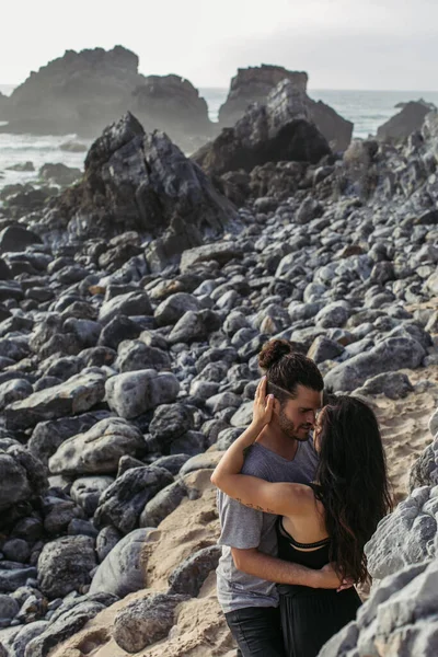 Tattooed woman hugging bearded man on rocky beach in portugal — Stock Photo