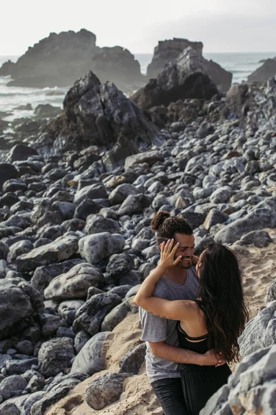 Tattooed woman hugging happy bearded man on rocky beach in portugal — Stock Photo