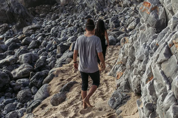Вид сзади мужчины, идущего за женщиной на скальном пляже в Португале — стоковое фото