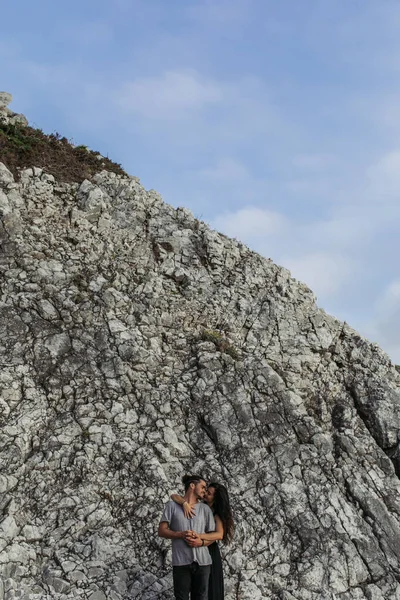 Brunette woman hugging bearded boyfriend while holding hands near rocks — Stock Photo