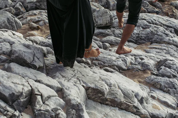 Vista recortada de hombre y mujer descalzos con brazalete de tobillo caminando sobre rocas - foto de stock