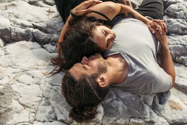 Top view of man hugging tattooed girlfriend while lying on rocks and holding hands — Stock Photo