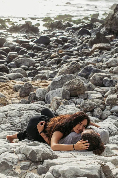 Tattooed woman and man lying together on stones near ocean — Stock Photo